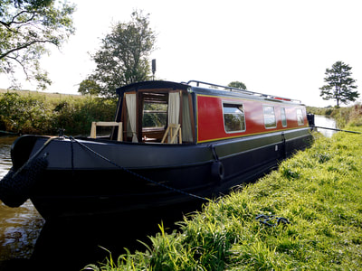 Side view of a red and blue hire narrowboat moored on the towpath of the Lancaster canal