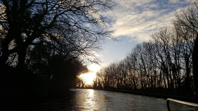 dusk on the Lancaster canal in winter with sun setting behind the trees beneath a blue sky with scattered clouds