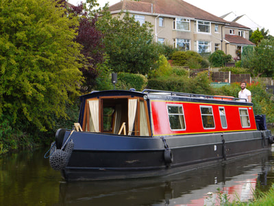 Side view of a red and blue, semi traditional hire narrowboat cruising on the Lancaster canal